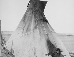 A young Oglala girl sitting in front of a tipi